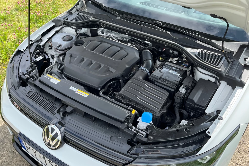 Z poczciwego 2.0 TSI udało się wykrzesać aż 300 KM oraz 400 Nm. Otwarta maska samochodu ukazująca nowoczesny silnik z logo Volkswagena, widoczne elementy układu chłodzenia, akumulator, pokrywa silnika i inne podzespoły mechaniczne.