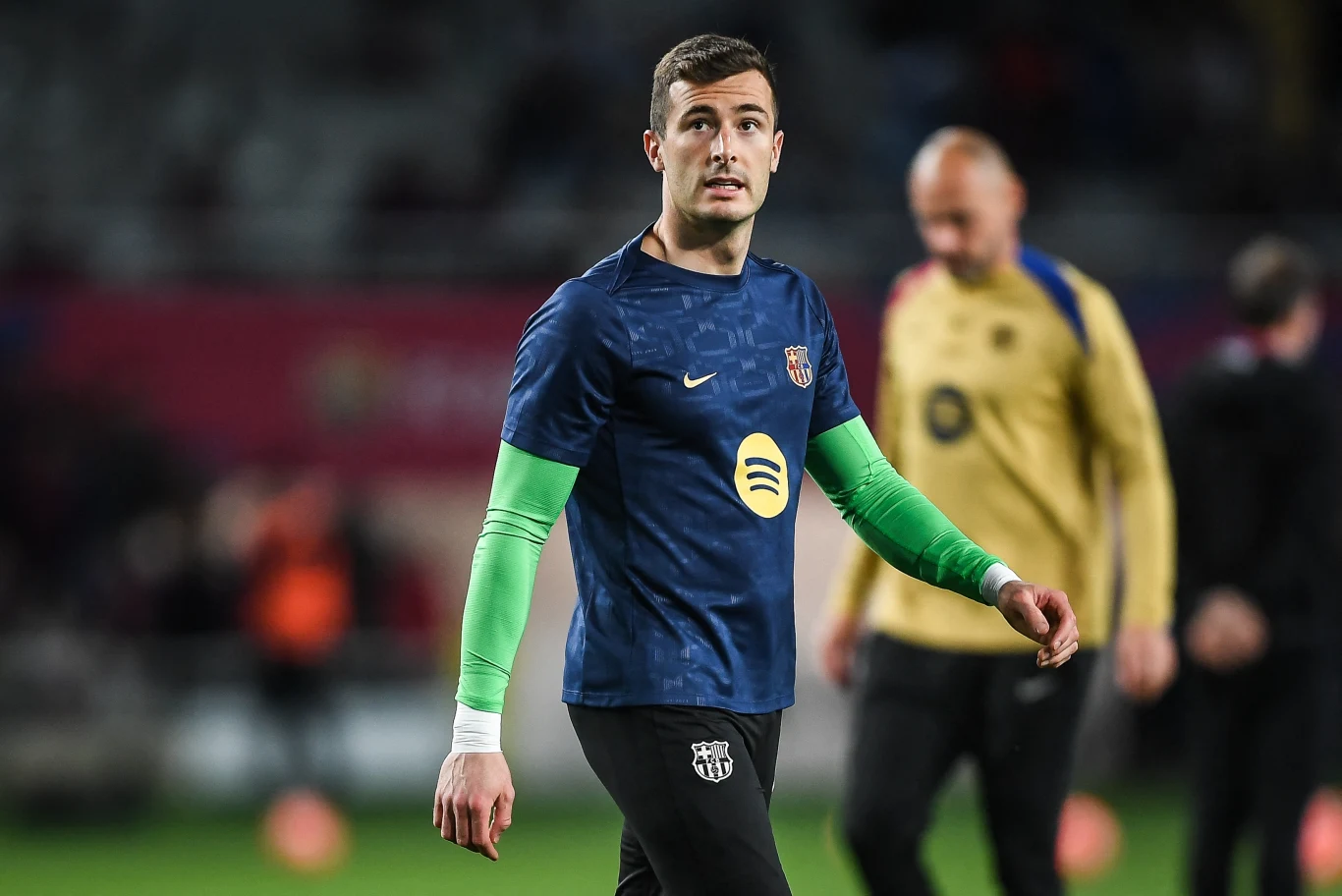 Inaki Pena Piłkarz w niebieskiej koszulce z zielonymi rękawami stoi na murawie stadionu podczas rozgrzewki, w tle rozmazane sylwetki innych zawodników.