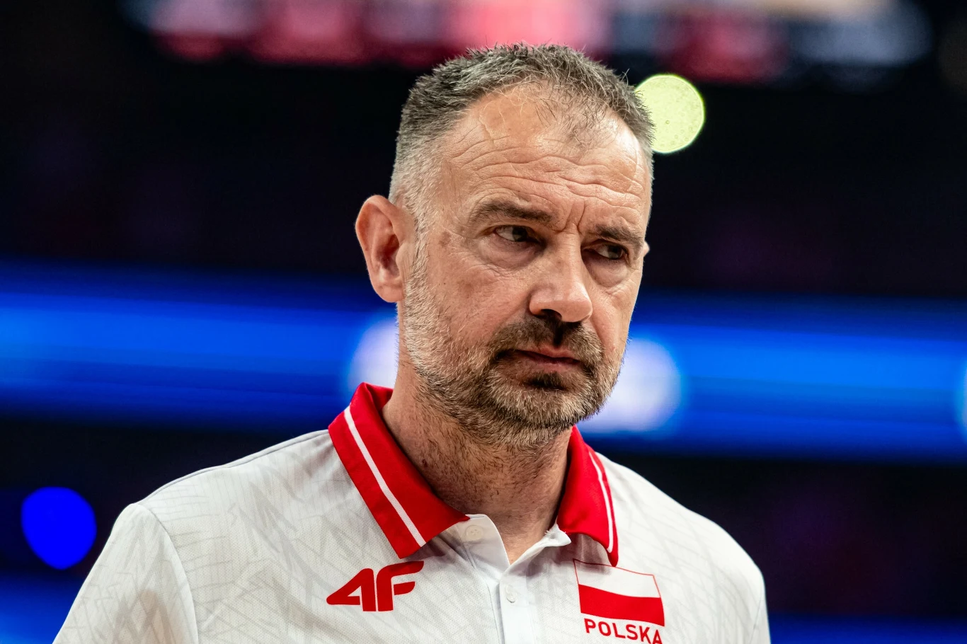 Mężczyzna w średnim wieku w sportowej koszulce z napisem POLSKA, poważny wyraz twarzy, wyraziste światło w tle, wyeksponowany logotyp 4F na koszulce.