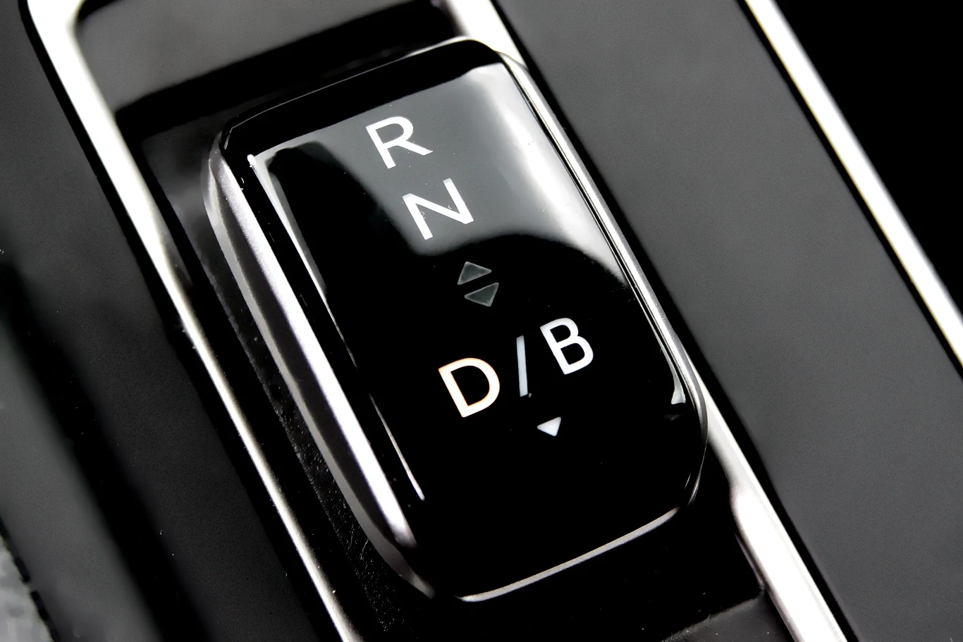 Czarny selektor trybów jazdy automatycznej skrzyni biegów z jasno oznaczonymi pozycjami R, N, D/B, znajdujący się w nowoczesnym wnętrzu pojazdu.