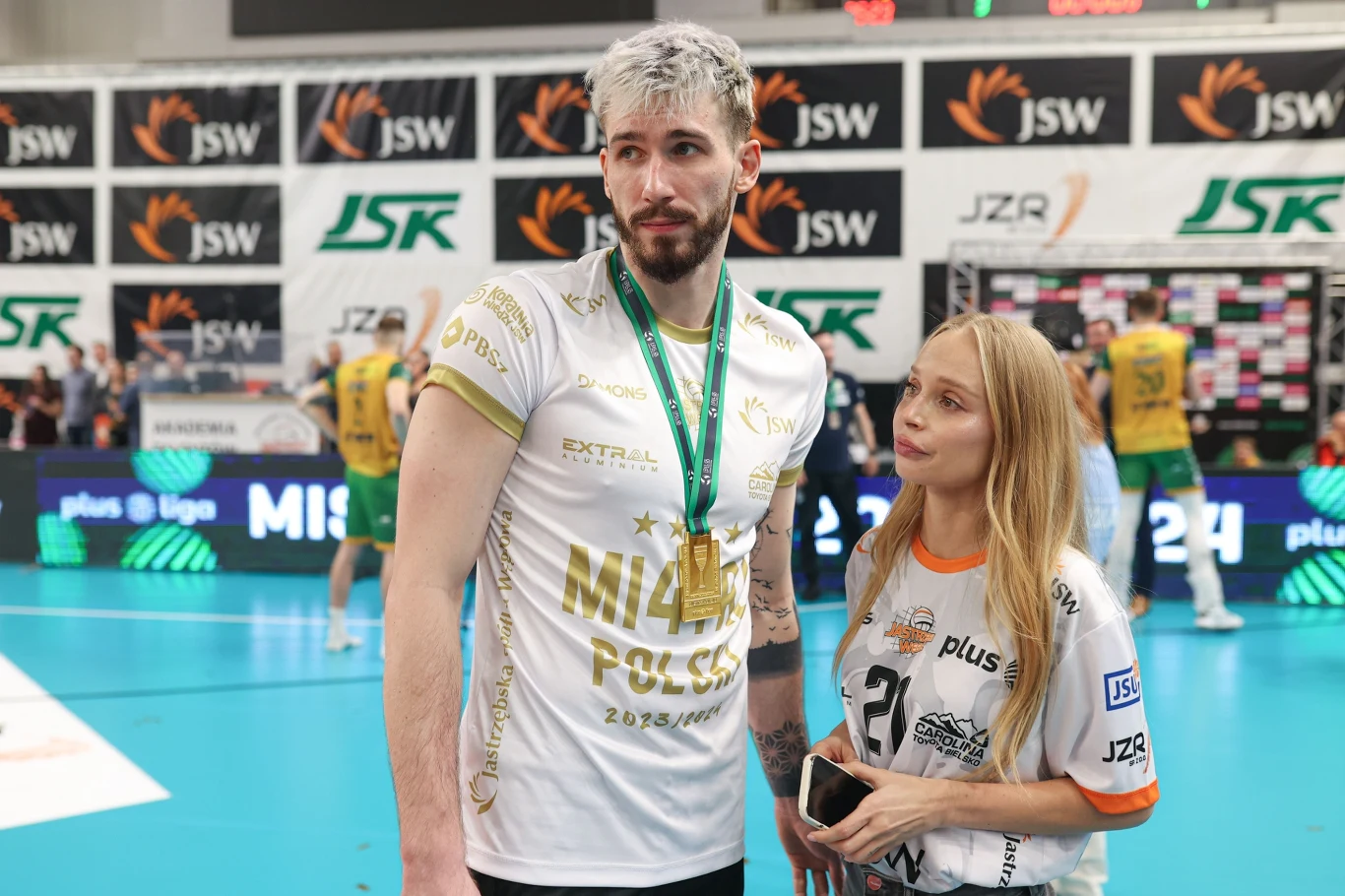 Tomasz Fornal i Sylwia Gaczorek, 2024 rok Zawodnik siatkarski z medalem na szyi oraz młoda kobieta w koszulce sportowej stoją razem na hali sportowej, w tle widoczna dekoracja z logo sponsorów i inni uczestnicy wydarzenia.