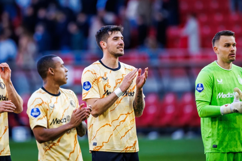 Jakub Moder Kilku piłkarzy w żółtych strojach drużyny sportowej stoi razem na boisku, klaszcząc w dłoniach, na dalszym planie widoczne puste czerwone trybuny stadionu.