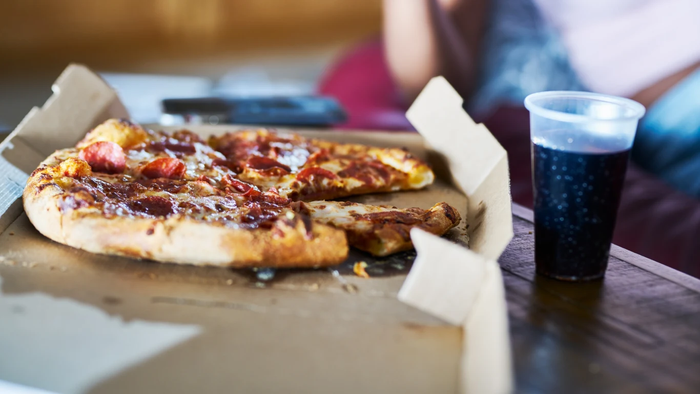 UE zakazuje niektórych opakowań w ramach regulacji PPWR Pudełko z kawałkami pizzy pepperoni i plastikowy kubek z ciemnym napojem na stole, UE zakazuje niektóre opakowania.