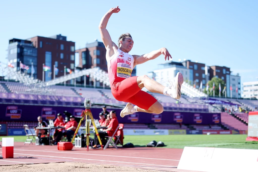 Hubert Trościanka, Tampere 2025 Lekkoatleta w biało-czerwonym stroju wykonuje skok w dal podczas zawodów na stadionie, w tle widoczne trybuny oraz sędziowie przy sprzęcie pomiarowym.