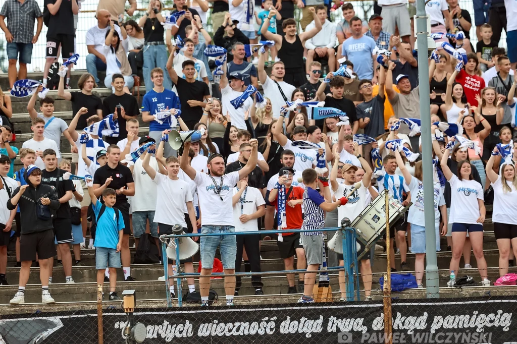 Autona Unia Tarnów Tłum entuzjastycznych kibiców na trybunach podnosi szaliki drużyny, wyraźnie świętuje wydarzenie sportowe, niektórzy mają megafony i bębny, widoczna jest energia i wspólnotowy duch.