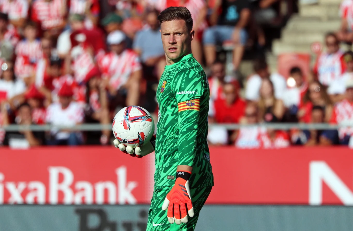 Marc-Andre ter Stegen Bramkarz w zielonym stroju z piłką do piłki nożnej w ręku na tle zamazanej publiczności na stadionie sportowym.