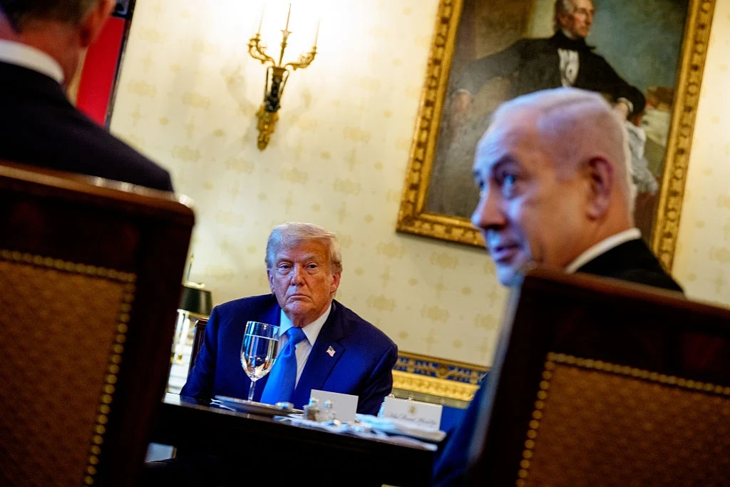 Donald Trump nakrzyczał na premiera Izraela, Benjamina Netanjahu Trzech mężczyzn siedzących przy stole w eleganckim wnętrzu, w tle portret mężczyzny w historycznym stroju oraz ozdobny kinkiet, głównym punktem jest mężczyzna pośrodku z poważnym wyrazem twarzy, przed którym stoi kieliszek z wodą.