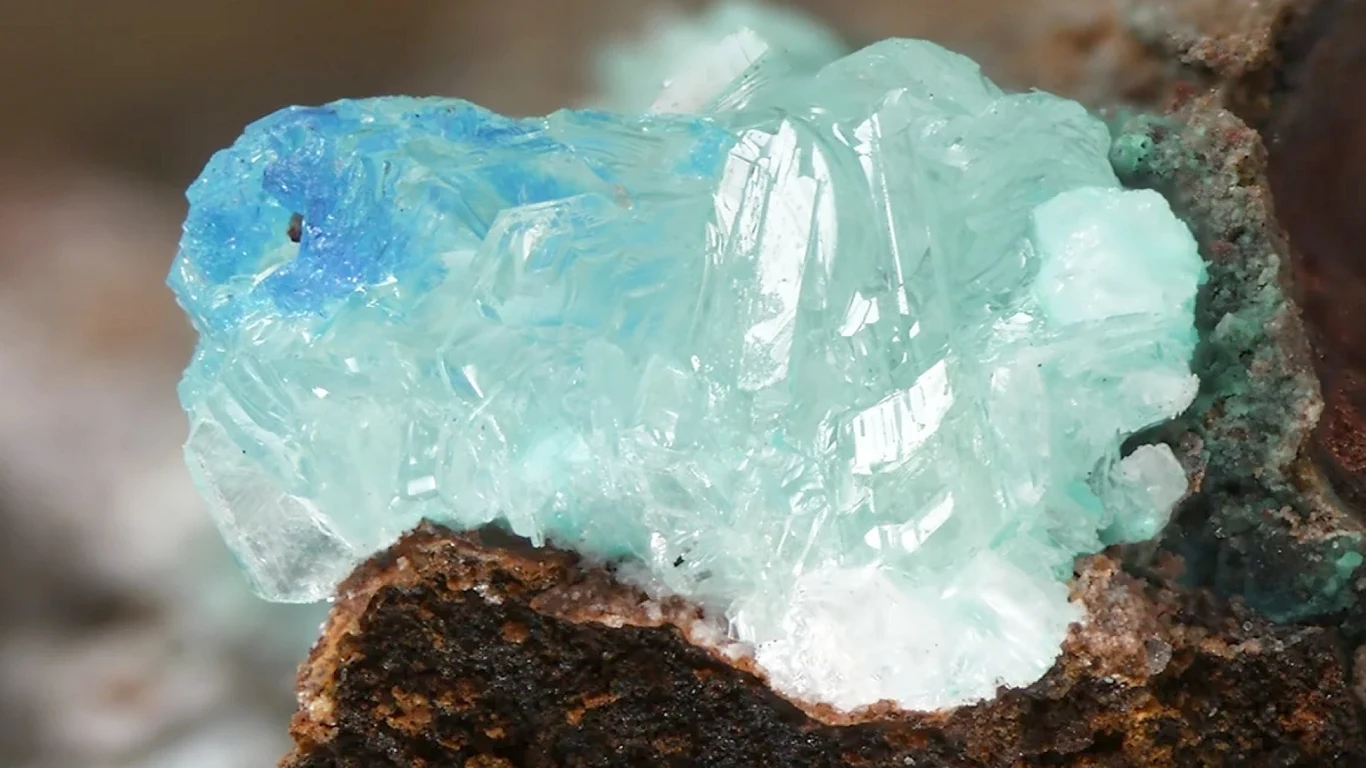 Tajemnicza substancja odkryta na Marsie Niebiesko-turkusowy kryształ minerału wyrośnięty na brązowej, chropowatej powierzchni skały, struktura minerału jest przezroczysta i połyskująca.