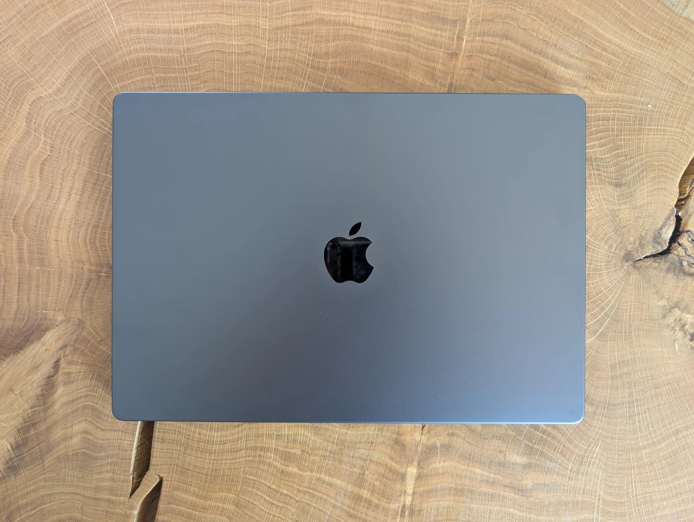 MacBook Pro 16" z M4 Pro Zamknięty laptop marki Apple w kolorze szarym umieszczony na drewnianym, nieregularnym blacie o wyraźnych słojach.