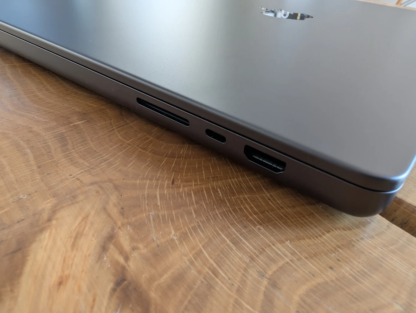 MacBook Pro 16" z M4 Pro Zbliżenie na zamkniętą obudowę laptopa umieszczonego na drewnianym blacie, widoczne różne porty, w tym HDMI, USB-C oraz czytnik kart SD.