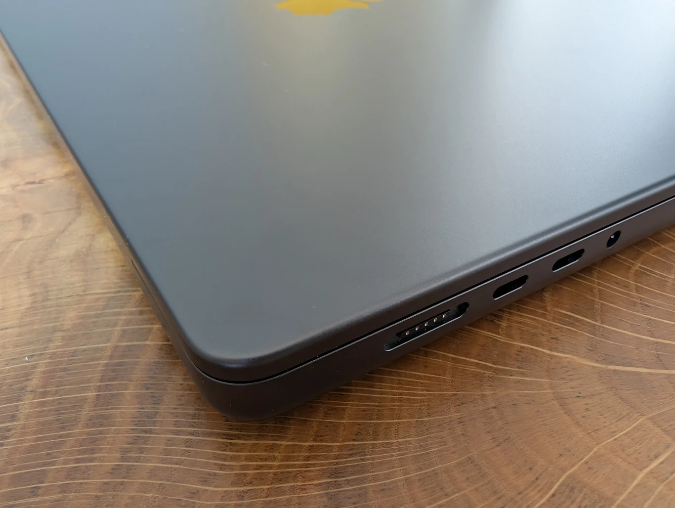 MacBook Pro 16" z M4 Pro Zamknięty laptop w kolorze ciemnoszarym leży na drewnianym blacie, widoczne są porty z boku obudowy, w tym gniazdo ładowania oraz porty USB-C.