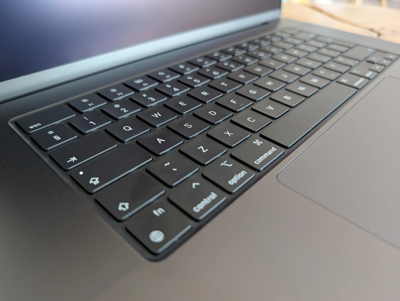 MacBook Pro 16" z M4 Pro Czarna klawiatura laptopa z wyraźnie widocznymi przyciskami i fragmentem gładzika, ekran częściowo otwarty.