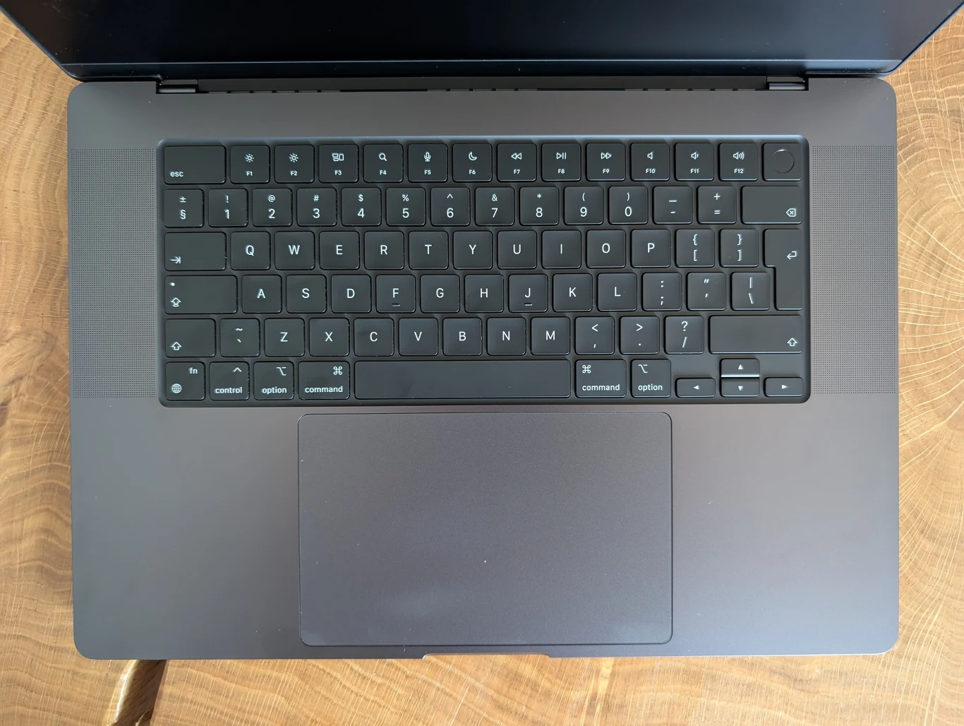 MacBook Pro 16" z M4 Pro Nowoczesny laptop o ciemnej obudowie z klawiaturą QWERTY, widoczny z góry, umieszczony na drewnianym blacie.