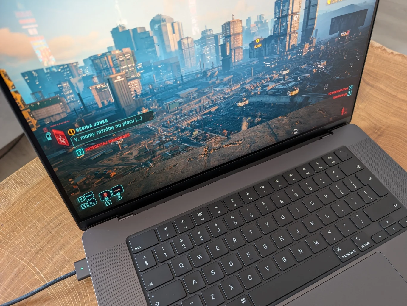 MacBook Pro 16" z M4 Pro Laptop z uruchomioną grą komputerową osadzoną w futurystycznym mieście, widoczny ekran prezentuje szczegółową panoramę miejską z wieloma wieżowcami, licznymi elementami interfejsu użytkownika i opcjami dialogowymi w grze.