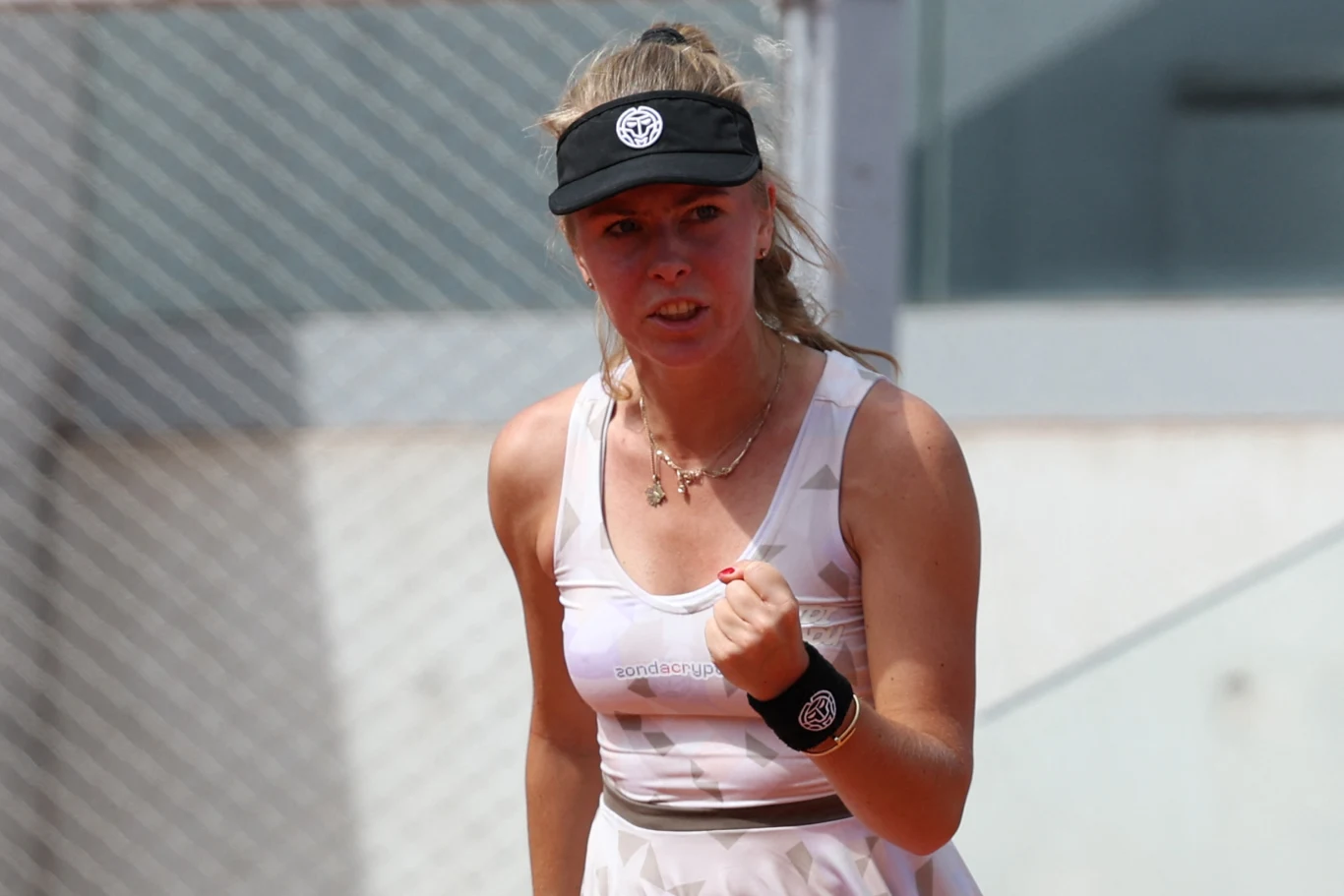 Magdalena Fręch Młoda tenisistka w białej sukience sportowej i czapce z daszkiem wykonuje gest zaciśniętej pięści, wyrażając determinację oraz koncentrację na korcie tenisowym.