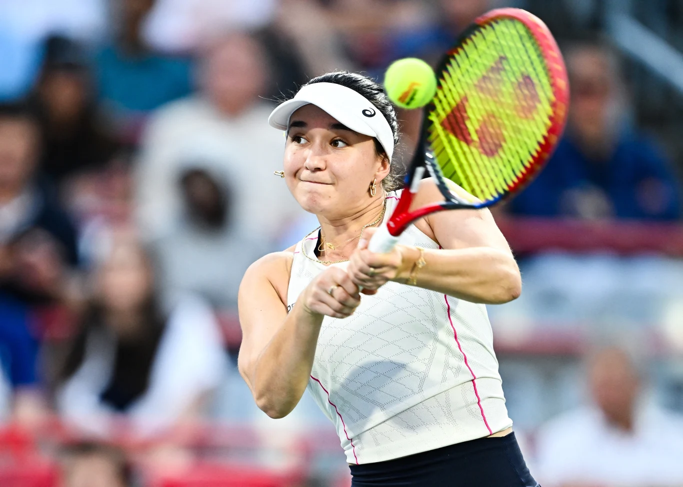 Tenisistka uderzająca piłkę rakietą podczas meczu na korcie, skupienie na twarzy zawodniczki, dynamiczny moment gry.