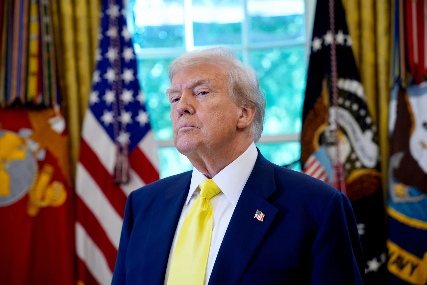 Donald Trump zabiega o nagrodę Nobla. Media: To grozi powtórką z Monachium w 1938 roku Mężczyzna w garniturze z żółtym krawatem stoi w eleganckim wnętrzu z flagami Stanów Zjednoczonych i innych instytucji w tle.