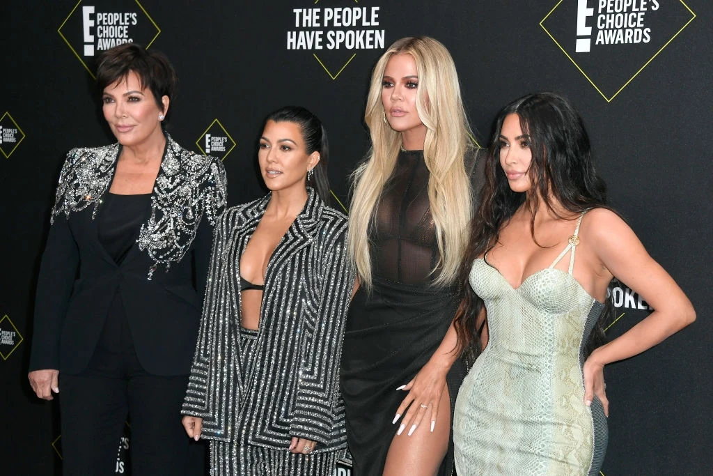 Kirs Jenner z córkami: Kourtney, Kim, Khloé Kardashian Cztery kobiety pozujące razem podczas uroczystej gali, ubrane w efektowne kreacje wieczorowe, na tle ściany z logotypami wydarzenia People’s Choice Awards.