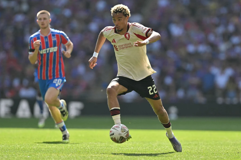 Hugo Ekitike Zawodnik drużyny piłkarskiej w jasnej koszulce z numerem 22 w dynamicznym biegu z piłką nożną na boisku, w tle drugi zawodnik w pasiastym stroju obserwuje sytuację.