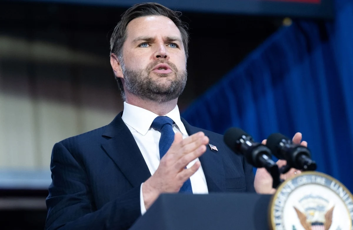 Wiceprezydent USA J.D. Vance Mężczyzna w garniturze i krawacie przemawia przy mównicy z mikrofonami, obok widoczne oficjalne godło Stanów Zjednoczonych, w tle granatowe zasłony.