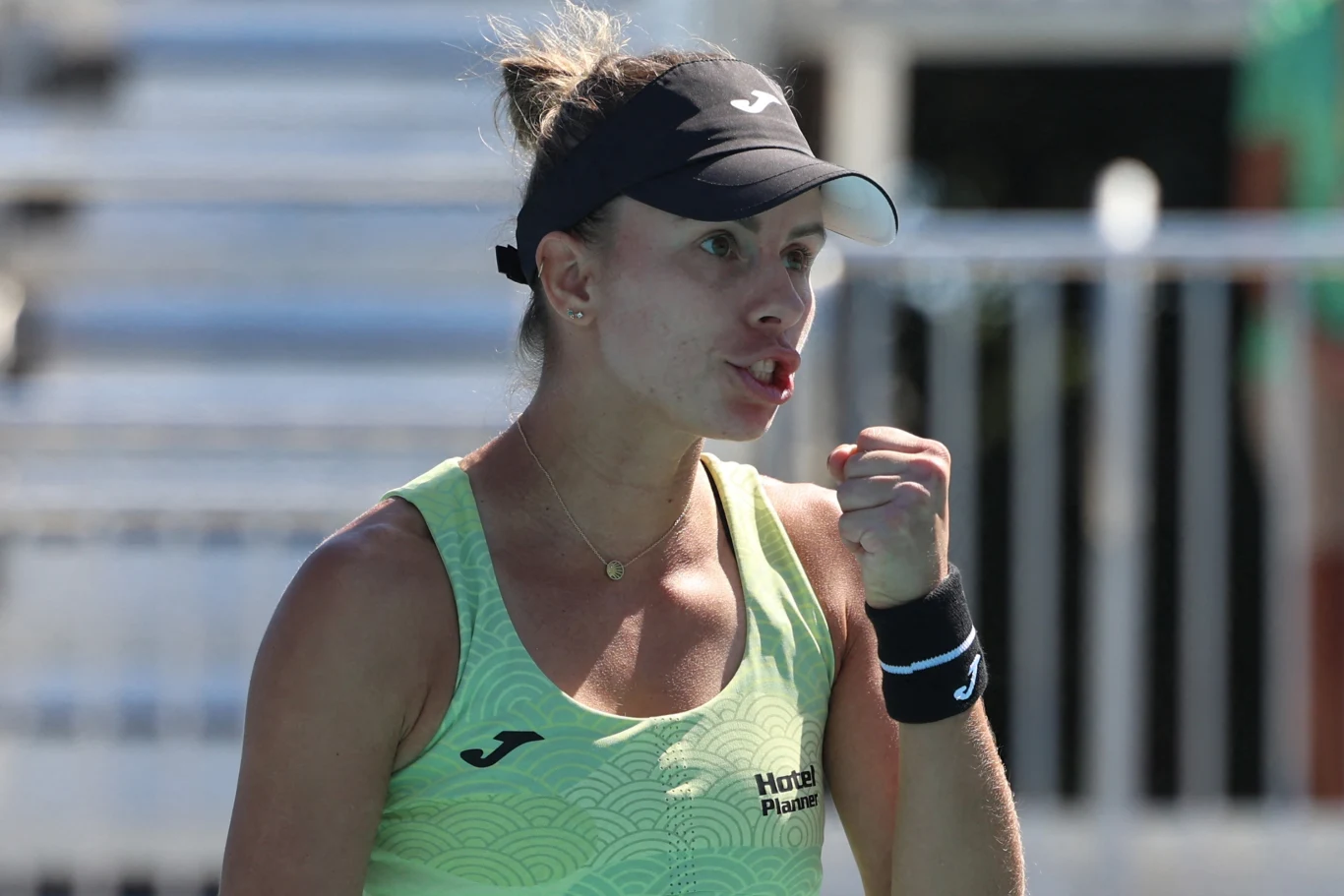 Kobieta w sportowym stroju i czapce z daszkiem unosi zaciśniętą pięść w geście triumfu, wyglądając na skupioną i pełną energii.