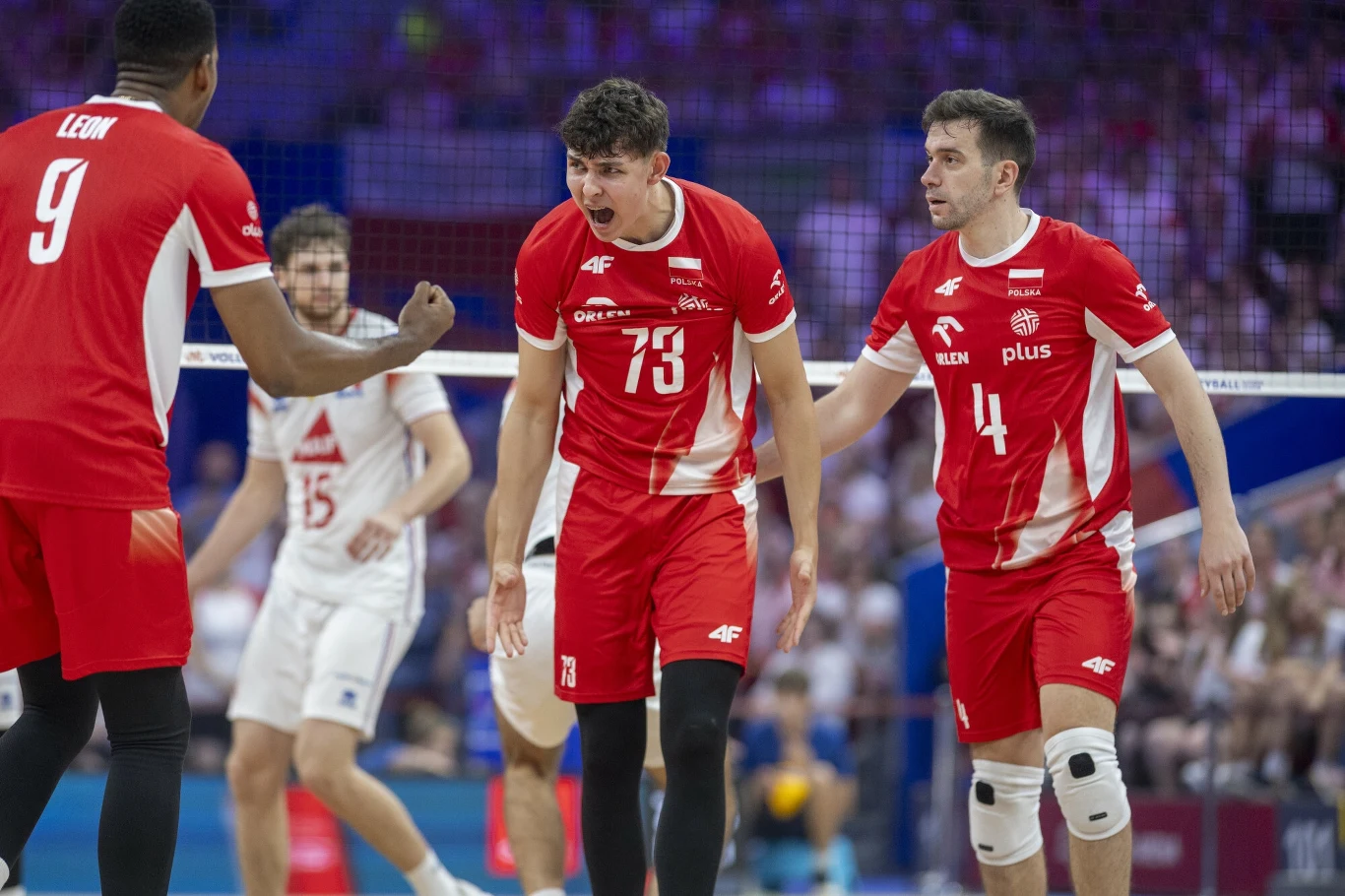 Jakub Nowak (z numerem 73) w reprezentacji Polski Grupa polskich siatkarzy w czerwonych strojach świętuje punkt na boisku podczas meczu siatkówki, w tle widoczni zawodnicy drużyny przeciwnej oraz publiczność.