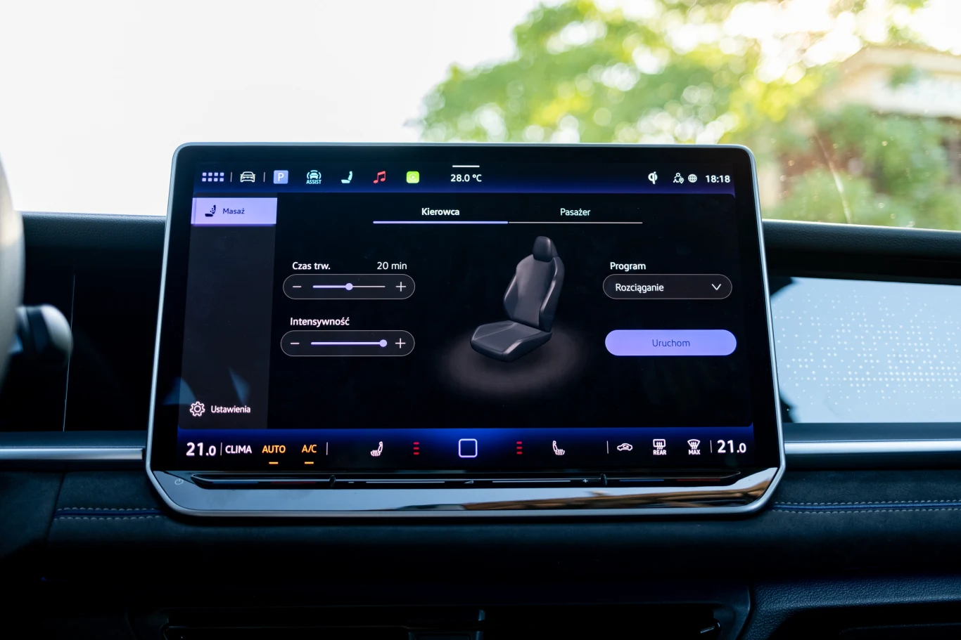 Kierowca i pasażer mogą skorzystać z kilku opcji masażu. Duży ekran dotykowy samochodu prezentujący ustawienia masażu fotela kierowcy, z widocznymi ikonami systemu multimedialnego oraz opcjami wyboru programu masażu, intensywności i czasu trwania; całość otoczona wnętrzem pojazdu, w tle delikatnie rozmazana ...