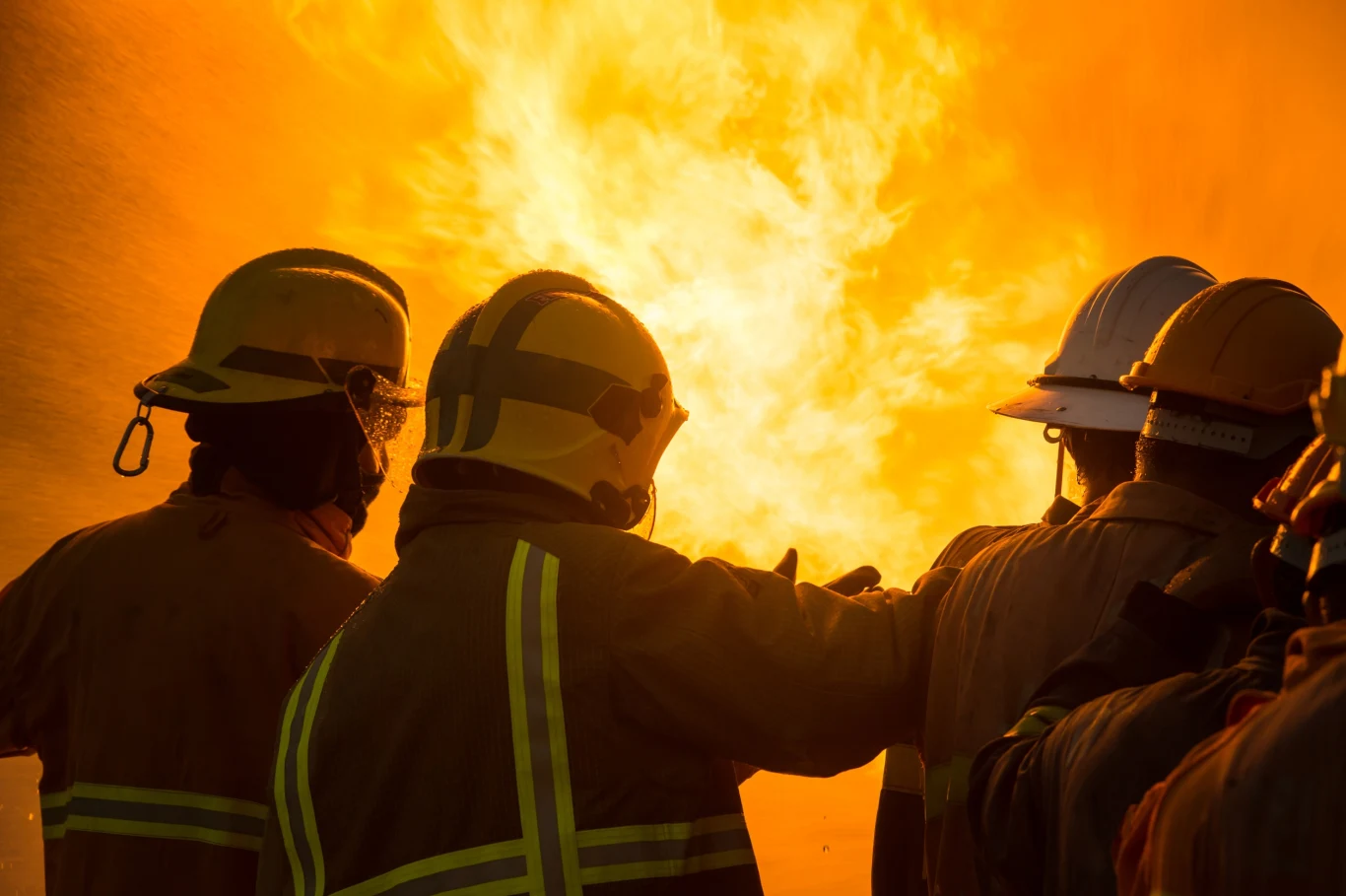 Popularny punkt turystyczny w Edynburgu stanął w ogniu. Na miejsce wysłano kilka wozów strażackich. Zdjęcie ilustracyjne. Grupa strażaków w żółtych kombinezonach i kaskach pracuje razem, walcząc z intensywnym ogniem; płomienie dominują tło, rozświetlając scenę pomarańczowym blaskiem.