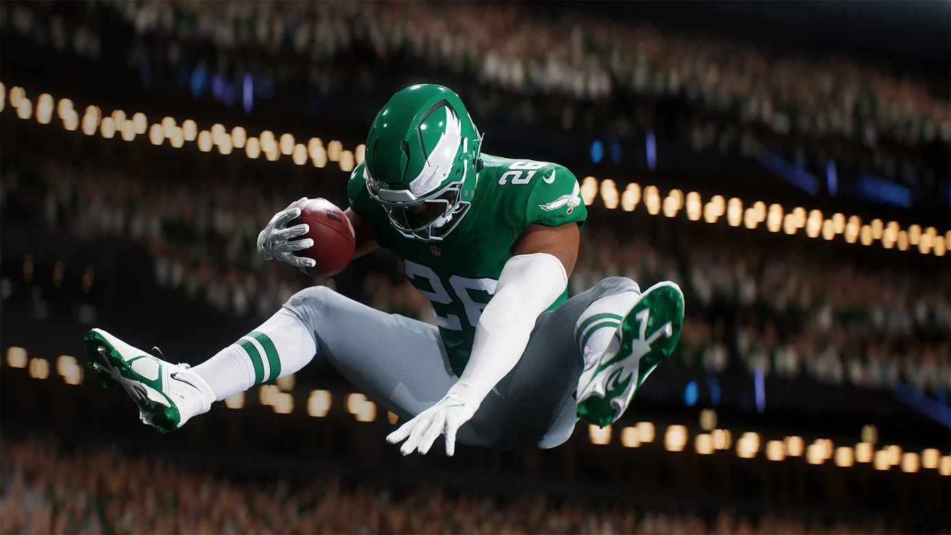 Madden NFL 26 Zawodnik futbolu amerykańskiego w zielonym stroju i kasku, unoszący się w powietrzu z piłką w jednej ręce, dynamiczne oświetlenie stadionu w tle, skupienie na akcji sportowej.