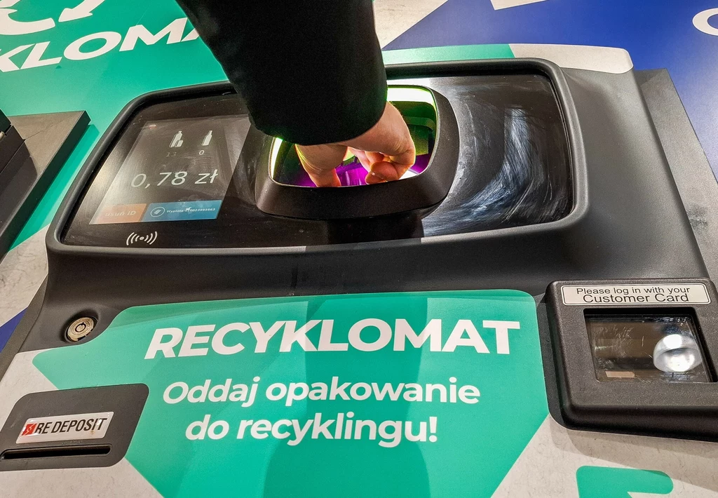 Osoba wkłada plastikową butelkę do recyklomatu, na ekranie widoczna jest informacja o zwrocie pieniędzy, a na maszynie instrukcja zachęcająca do recyklingu opakowań.