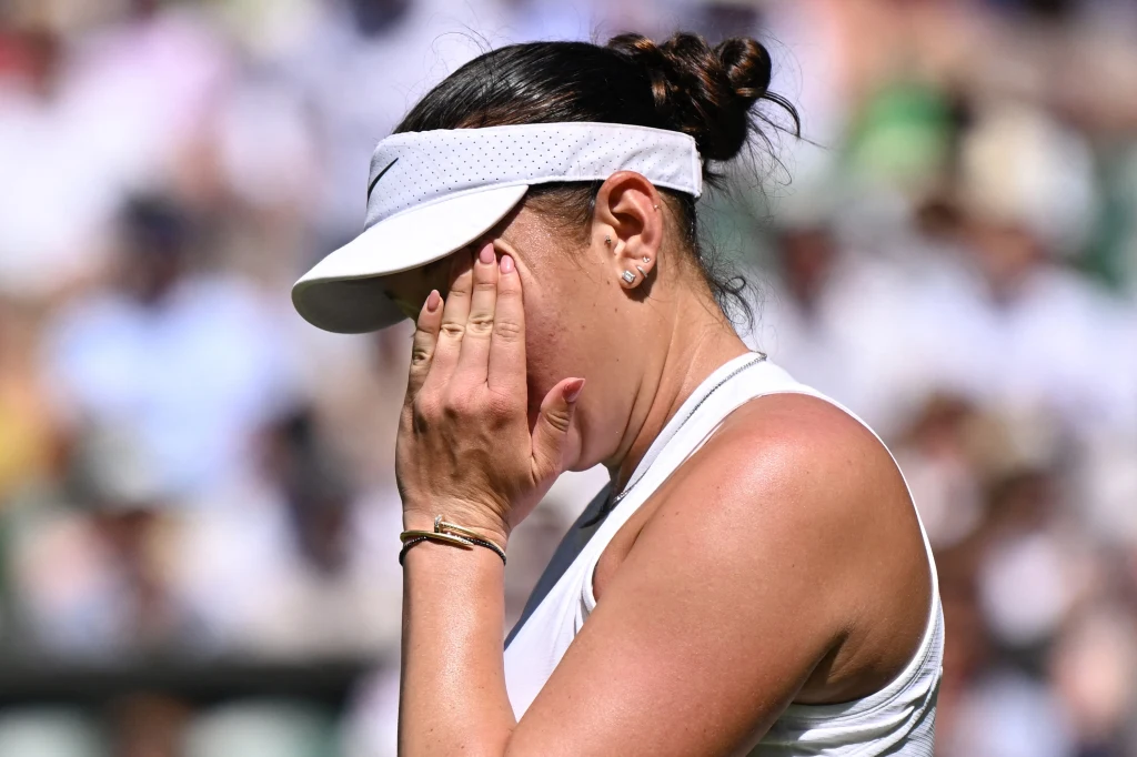 Amanda Anisimova Zawodniczka tenisowa w białym stroju i białej opasce na głowie trzyma rękę na twarzy, wyrażając silne emocje, tło rozmyte z widoczną publicznością.
