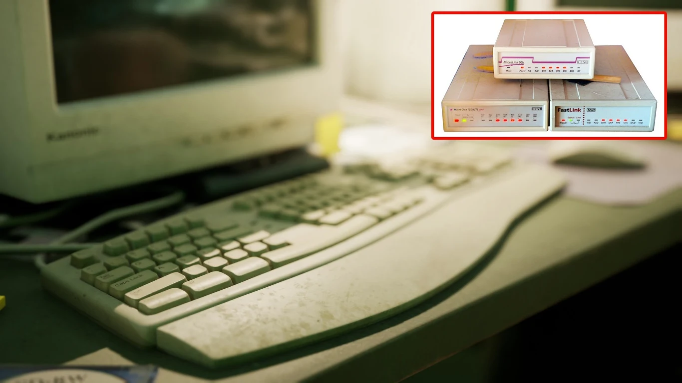 Tradycyjne modemy telefoniczne dial-up wydawały charakterystyczny dźwięk łączenia z internetem. Do dziś korzystają z nich setki tysięcy ludzi Stary monitor komputerowy wraz z klawiaturą stoi na biurku, w górnym rogu widoczne powiększenie starego modemu z diodami kontrolnymi.