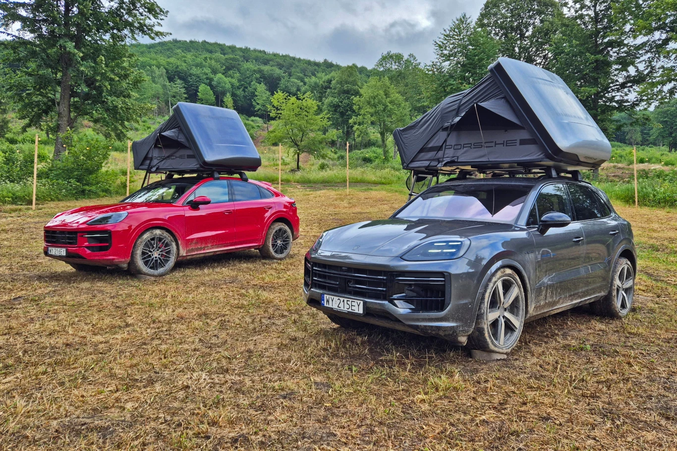 Porsche Cayenne z namiotem dachowym miałem okazję testować w Bieszczadach Dwa samochody Porsche SUV zaparkowane na polanie, każdy z nich wyposażony w dachowy namiot rozstawiony do spania; otoczenie stanowią drzewa i zielone wzgórza w tle.