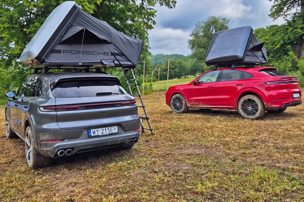 Dwa samochody marki Porsche z zamontowanymi na dachach namiotami w terenie zielonym, jeden pojazd srebrny, drugi czerwony, oba stoją na trawie w otoczeniu drzew i mają rozłożone schodki prowadzące do namiotów.