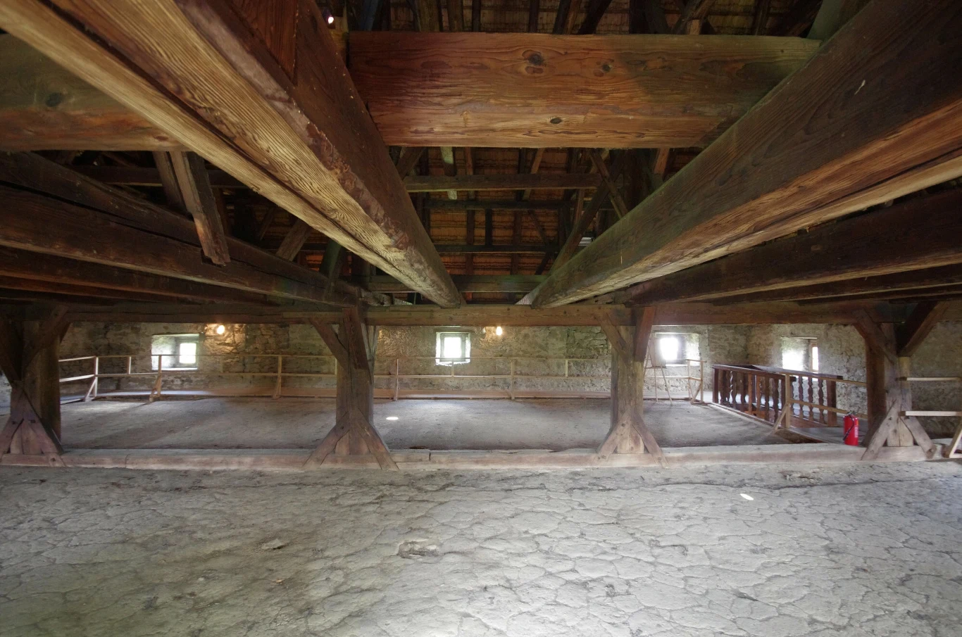 Wieża w Siedlęcinie to wyjątkowy zabytek na Dolnym Śląsku. Duża, przestronna sala z masywnymi drewnianymi belkami podtrzymującymi dach i kamienną podłogą, po bokach widoczne są niewielkie okna wpuszczające światło dzienne, w tle znajduje się drewniana balustrada.