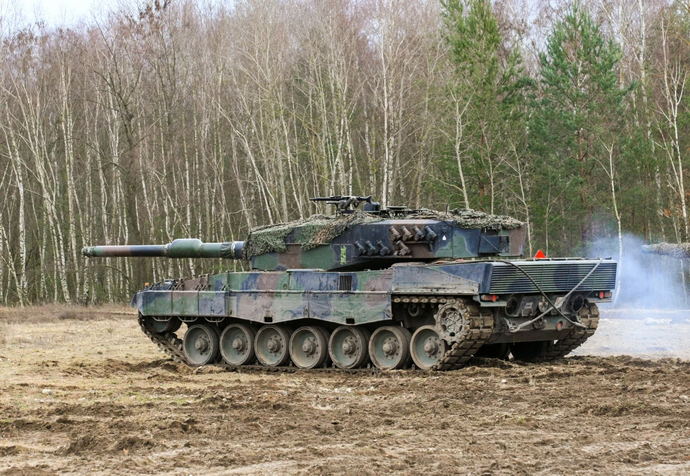 Czołg Leopard 2 to prawdziwa legenda. czołg Leopard 2 w klasycznym kamuflażu zielono-brązowym poruszający się po błotnistym terenie na tle lasu wczesną wiosną