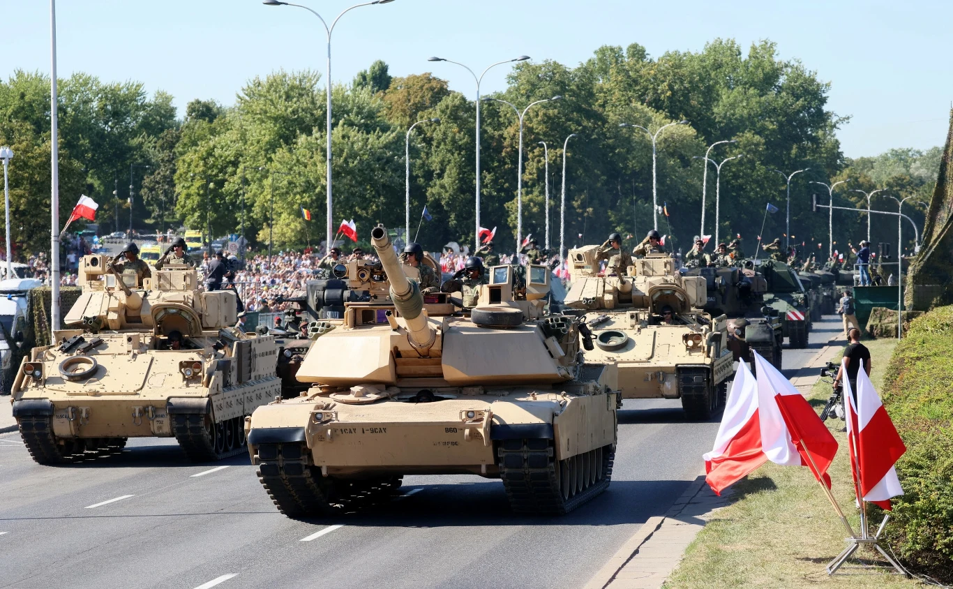 Amerykański Abrams M1 ma jeszcze większy apetyt niż Leopard 2 Kolumna nowoczesnych czołgów poruszająca się szeroką ulicą w otoczeniu licznych widzów i biało-czerwonych flag, z zielonymi drzewami w tle oraz obecnością żołnierzy na pojazdach.