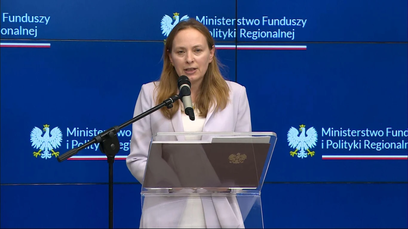 Minister Katarzyna Pełczyńska-Nałęcz złożyła wyjaśnienia w sprawie KPO Kobieta w jasnym stroju przemawia przy mównicy z mikrofonem na tle ściany z logotypami Ministerstwa Funduszy i Polityki Regionalnej oraz godłem Polski.