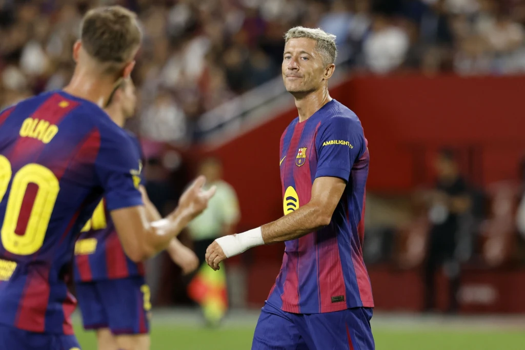 Robert Lewandowski Piłkarz w stroju FC Barcelony na boisku podczas meczu, wyrażający zadowolenie lub lekką satysfakcję, obok niego drugi zawodnik zespołu z widocznym nazwiskiem na koszulce i rozmytym tłem trybun.