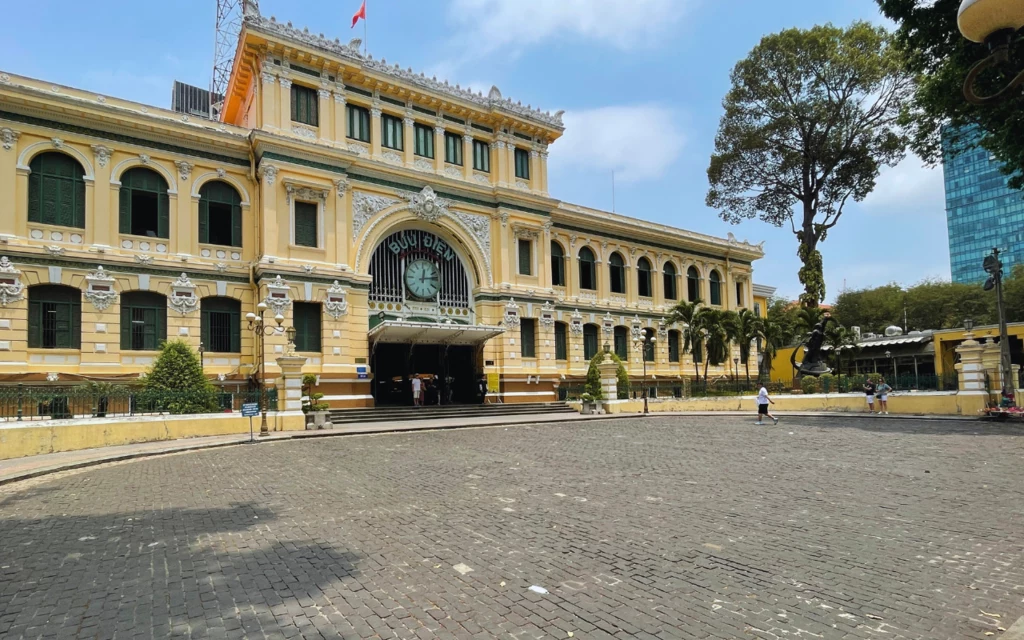 Budynek wciąż działającej poczty to jedna z architektonicznych perełek dawnej stolicy Zabytkowy budynek poczty centralnej w stylu kolonialnym z ozdobną fasadą, dużymi zielonymi oknami, ozdobnymi detalami architektonicznymi, przed wejściem brukowany plac, pojedyncze osoby spacerujące w oddali.