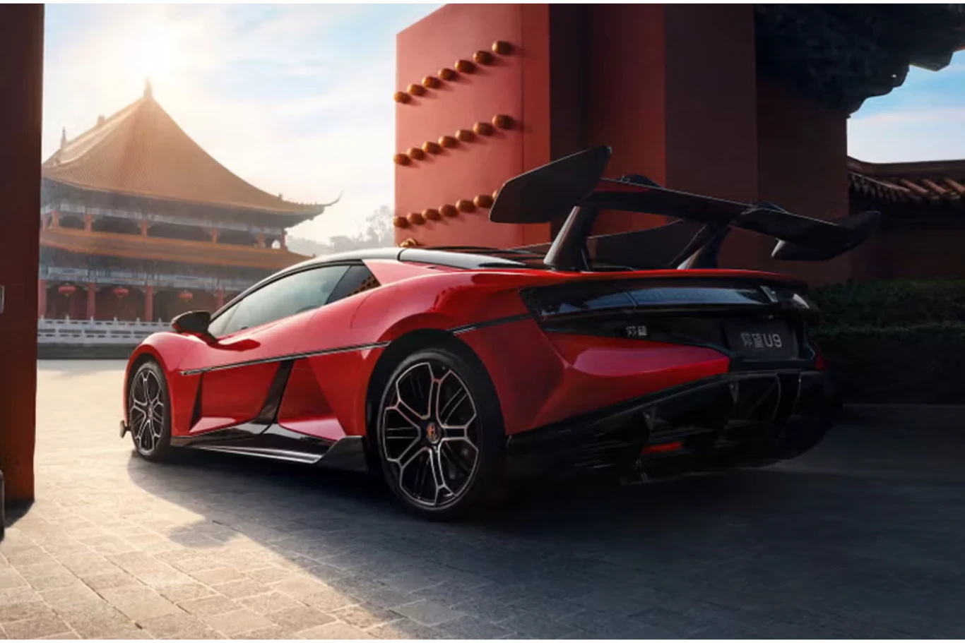 Inżynierowie postawili na opony w rozmiarze 325/30-20. Czerwony sportowy samochód z dużym spojlerem zaparkowany na tle tradycyjnej azjatyckiej architektury, w otoczeniu wysokich murów i charakterystycznych dachów.