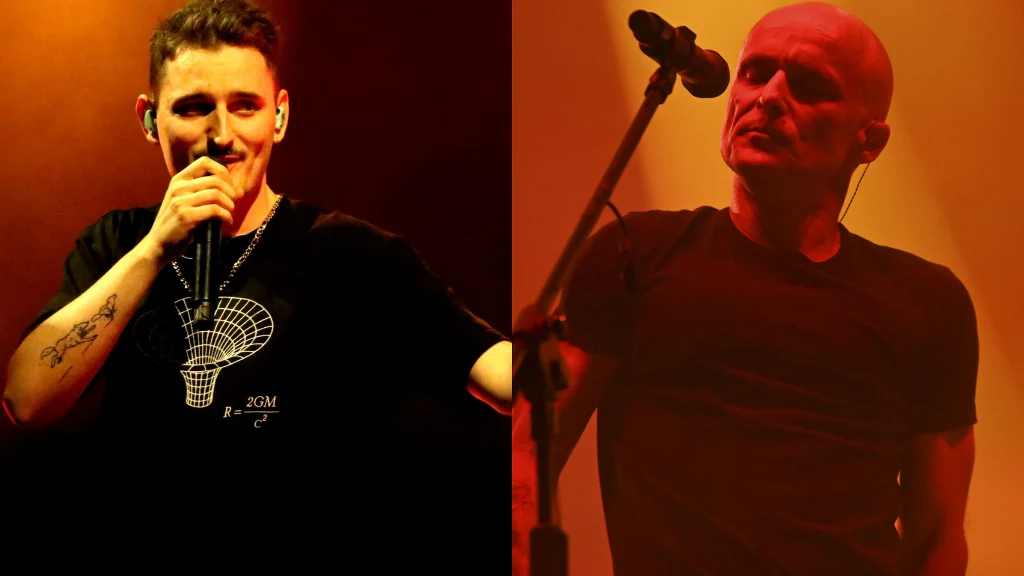 Dawid Podsiadło i Artur Rojek Dwóch mężczyzn śpiewa na scenie, każdy z mikrofonem, oświetleni ciepłym światłem, po lewej stronie młodszy mężczyzna w czarnej koszulce, po prawej starszy mężczyzna z ogoloną głową.