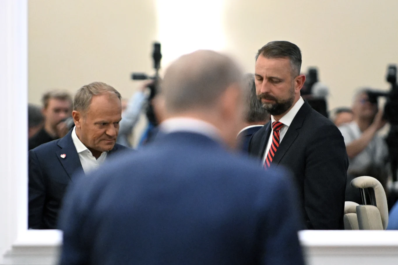 Rząd planuje zmiany w funkcjonowaniu Żandarmerii Wojskowej. Wszystko przez rosnące zagrożenie. Na zdjęciu premier Donald Tusk i minister obrony narodowej Władysław Kosiniak-Kamysz Dwóch mężczyzn w garniturach stoi obok siebie w jasnym pomieszczeniu, w tle widoczne kamery i osoby pracujące przy sprzęcie fotograficznym.