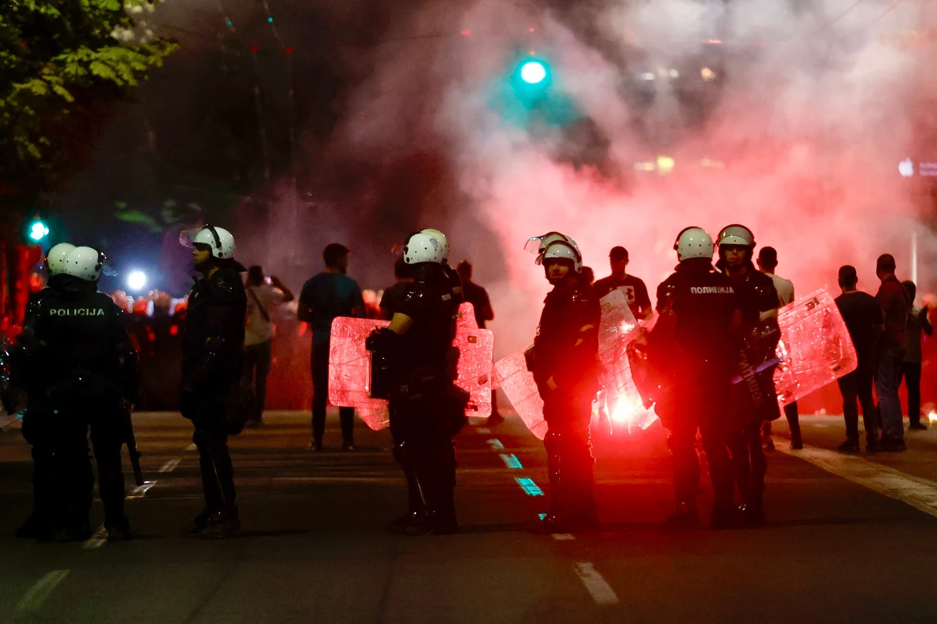 W Serbii manifestacje trwają od miesięcy. We wtorek doszło do kolejnej eskalacji i starć (zdjęcie z czerwcowych protestów) Uzbrojeni policjanci w hełmach i z tarczami blokują ulicę podczas zamieszek nocą, w tle widoczni demonstranci oraz duże ilości dymu i światło rac.