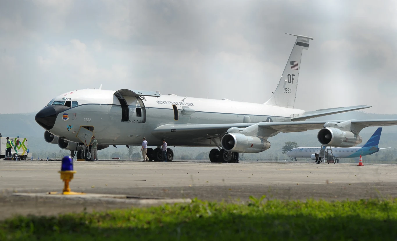 Boeing WC-135 Sił Powietrznych USA Samolot wojskowy z napisem United States Air Force ustawiony na płycie lotniska, w otoczeniu kilku osób oraz pojazdów obsługi, w tle widoczny drugi samolot cywilny.