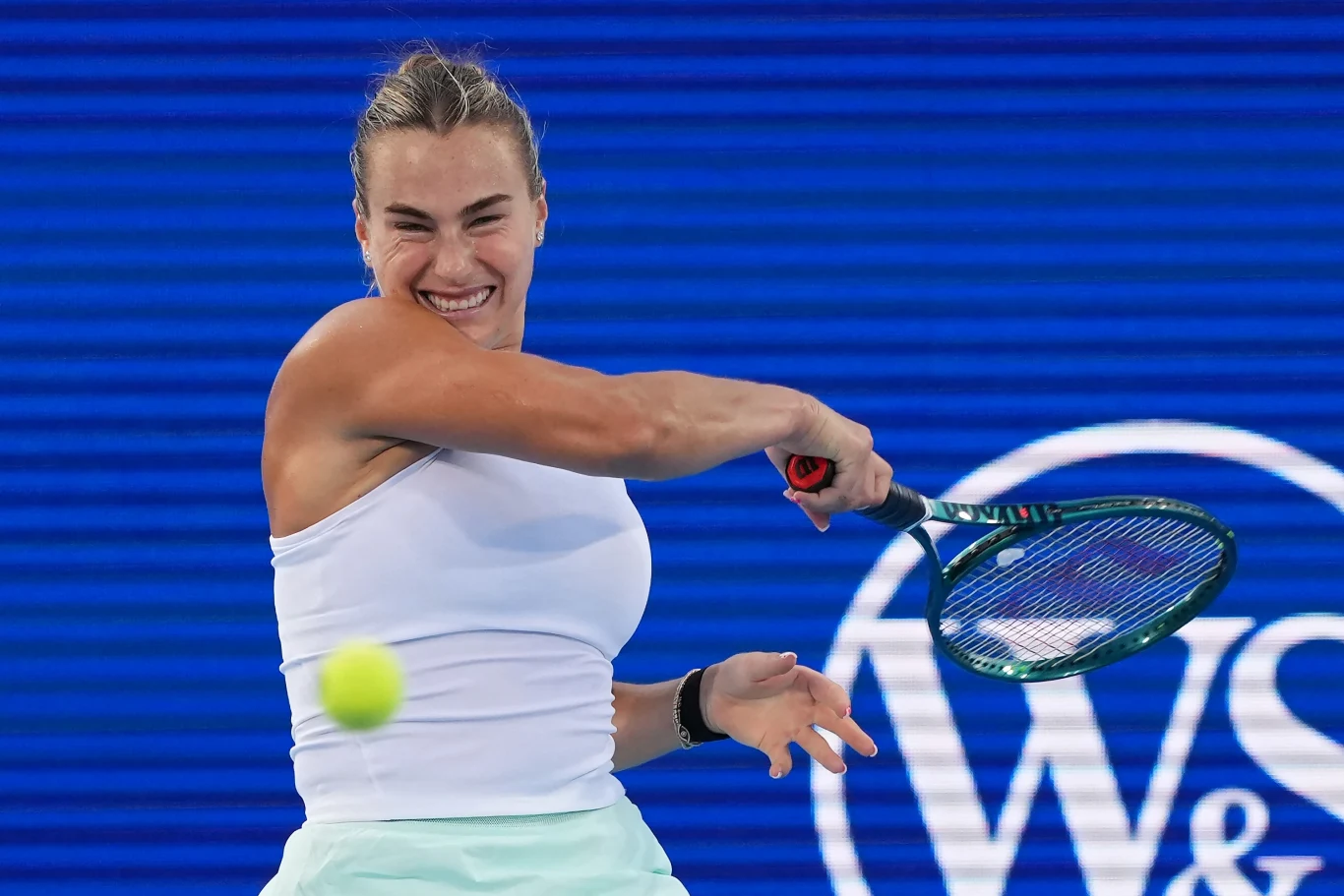 Aryna Sabalenka Tenisistka w białym stroju wykonuje uderzenie forehand podczas meczu na tle niebieskiego kortu i charakterystycznej tablicy W&S.