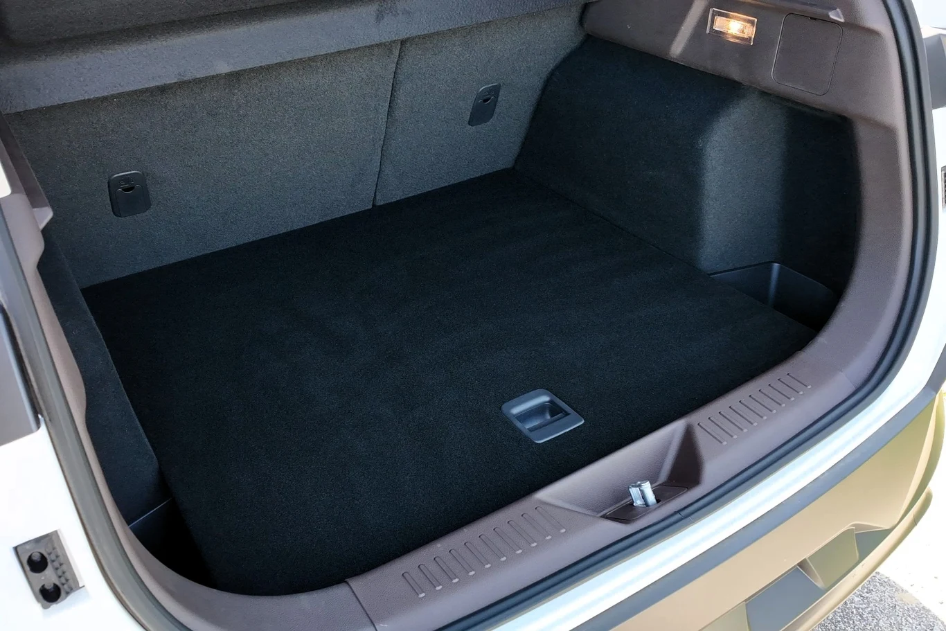 Pusta przestrzeń bagażnika samochodu z widocznym czarnym wykładzinowym wykończeniem oraz schowkiem w podłodze, oświetlenie wewnętrzne na jednej ze ścianek.