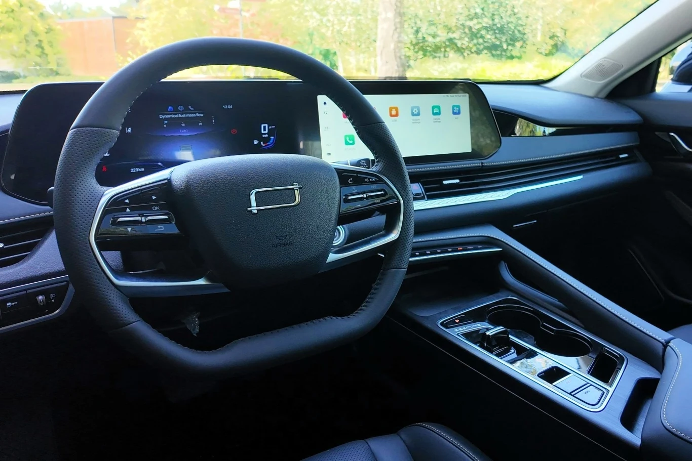 Kierownica auta, cyfrowy kokpit z ekranami i nowoczesna konsola środkowa w przestronnym, jasnym wnętrzu.