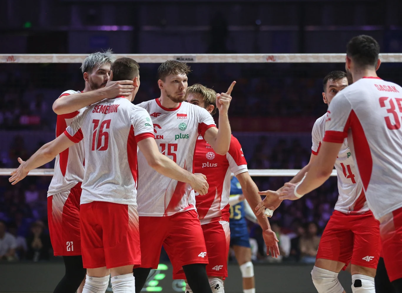 Siatkarze reprezentacji Polski podczas turnieju finałowego LN w Ningbo Polscy siatkarze ubrani w biało-czerwone stroje świętują zdobycie punktu podczas meczu, otoczeni przez kolegów z drużyny oraz przeciwników w tle, wyrażając emocje gestami i mimiką.