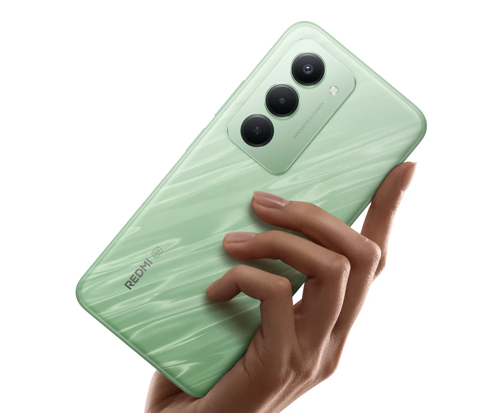 Jasnozielony smartfon marki Redmi trzymany w prawej dłoni, widoczne są trzy aparaty na tylnej obudowie oraz delikatny, błyszczący wzór na powierzchni telefonu.